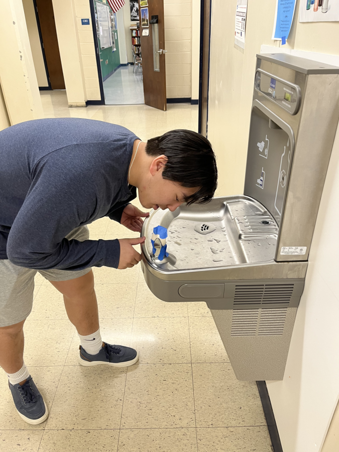 A student tears through blue tape (a supposed COVID-19 measure) around a water fountain to hydrate himself.