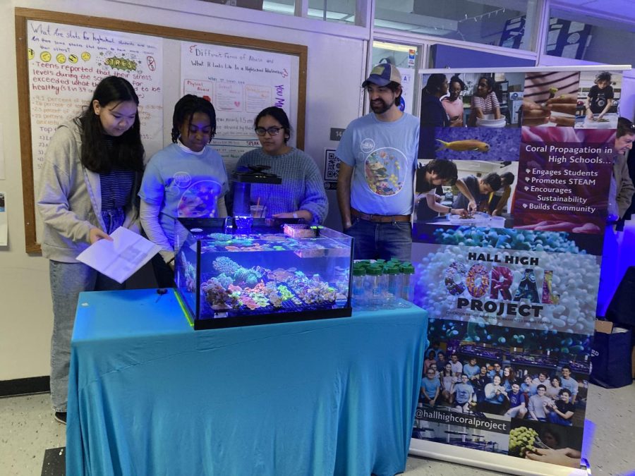 Club seniors Josephine Udell, Katherine Wright-Goodison, and Dhurshanie Ramlall stand behind their stand at Frag Farmers Market with the clubs proctor, Anthony Wasley, who is also Halls Oceanography teacher.