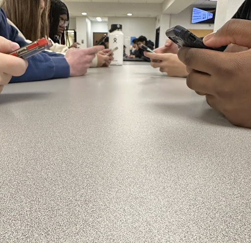 Students sitting at lunch table together on their phones.