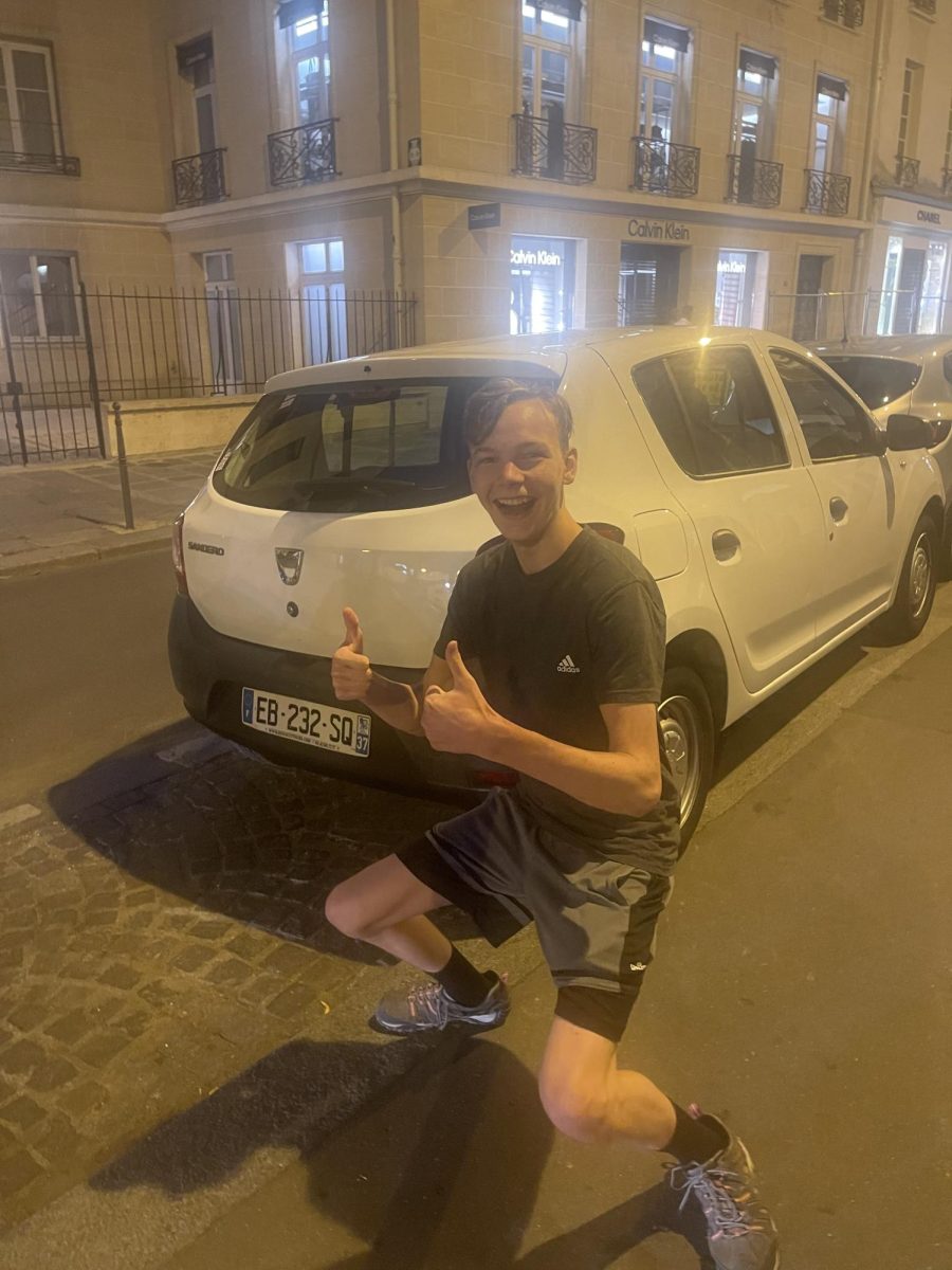 Ben Frey in the streets of Paris, standing normally in front of a Dacia Sandero