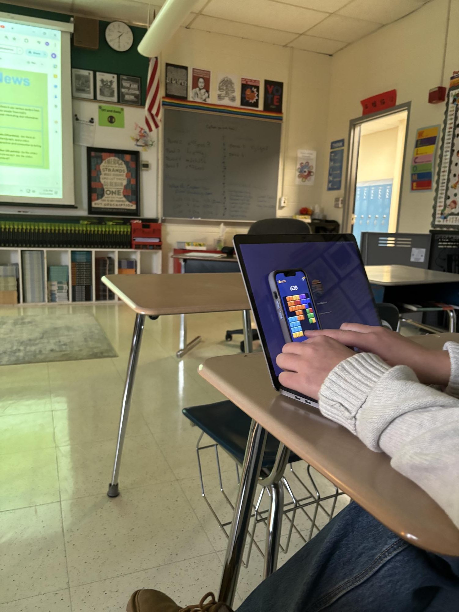 The image shows a student hiding her phone behind her computer.