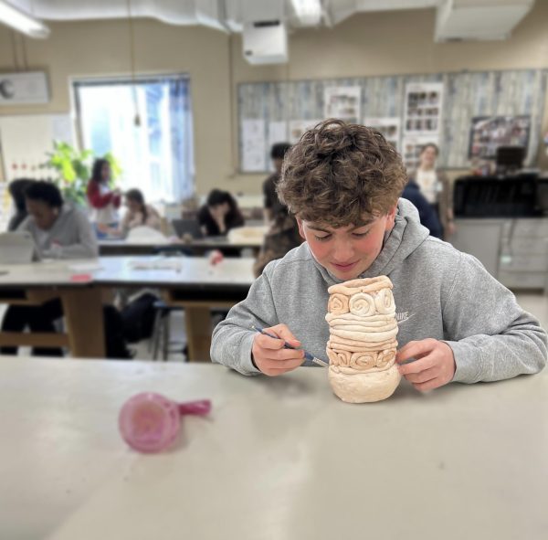 A freshman, Nate, glazes his completed piece designed to represent his identity. 