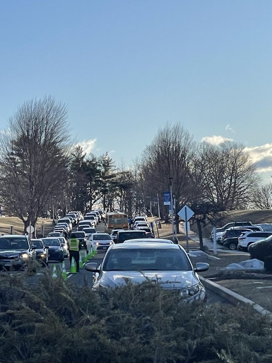 Typical morning traffic at Hall High School. A security guard is standing in the center to monitor and assist with the flow of traffic. A line of school buses are waiting for an opportunity to be able to leave, but are being blocked by cars in the drop-off line. Students rush from cars to make it to class in the three minutes before the bell rings, while their driver is forced to go back around and deal with the traffic all over again.
