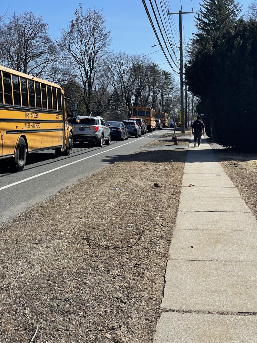 2:25pm bumper-to-bumper traffic on North Main St at the entrance to Hall High School. Traffic is growing as more cars and buses flood out of the school's entrance. Very few students choose to walk home as many more wait to be picked up. The line of cars grows as drivers fight for space on the very busy main road.  
