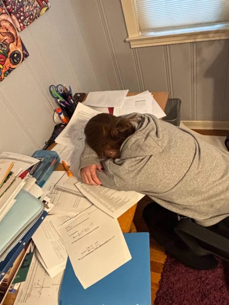 A student rests their head on a desk filled with schoolwork at their home in West Hartford, Conn., on Tuesday, Oct. 21, 2025. As extracurricular commitments pile up alongside academic demands, many students report feeling overwhelmed by the pressure to excel in every area.