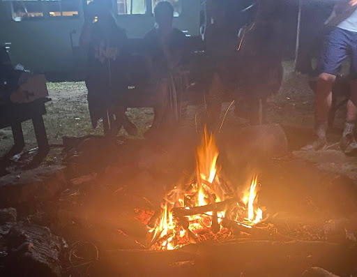 Teens sit around a campfire, embracing the outdoors. No matter how modern our world is, adventure remains available.